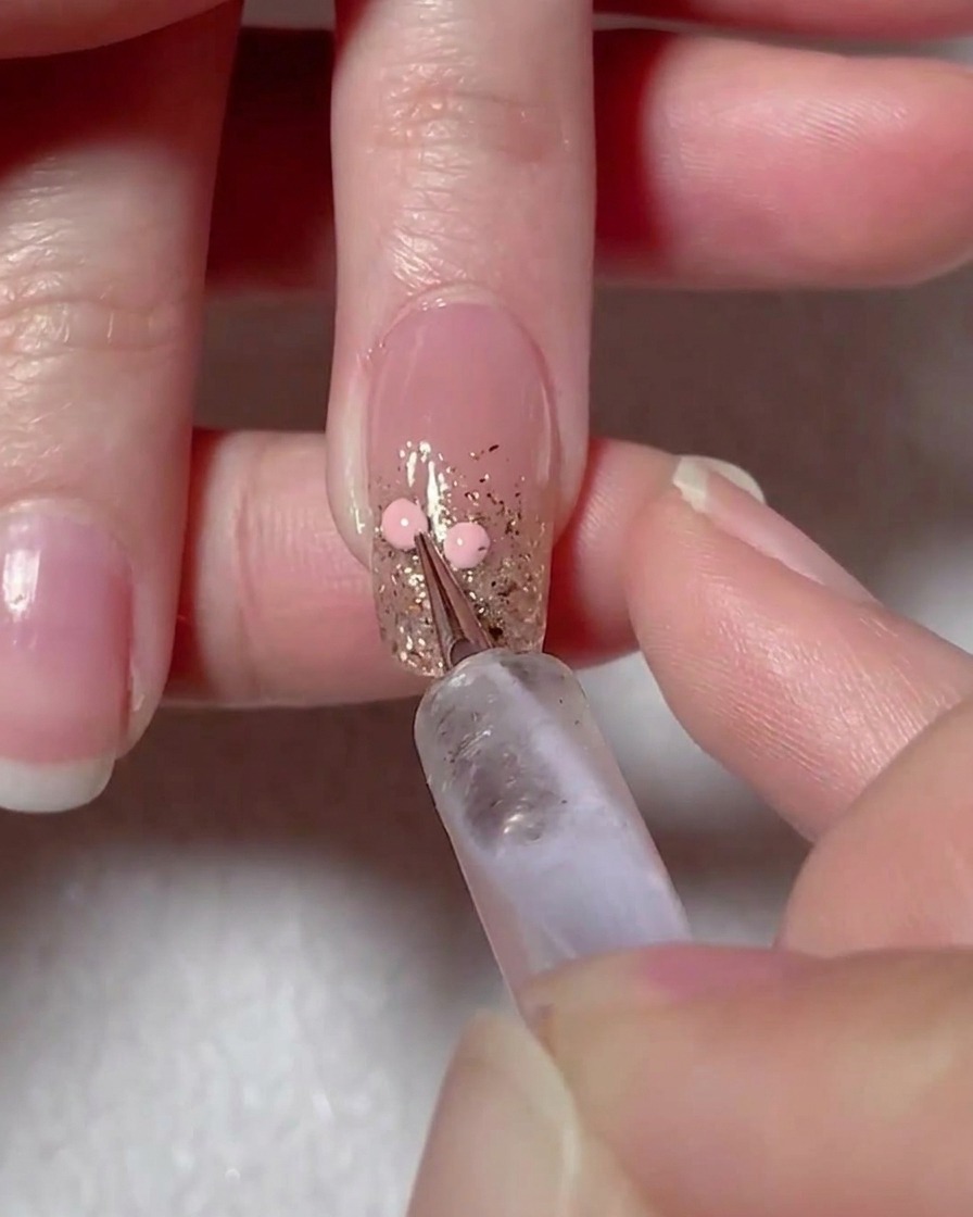 Uno strumento dotting posiziona due punti di gel rosa sulla superficie dellunghia per mappare un cuore.