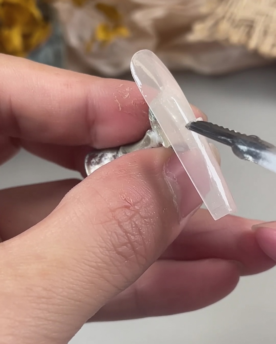 Una mano utilizza uno strumento per posizionare con precisione scaglie di glitter olografici e iridescenti sul gel bagnato e non polimerizzato di una tip.