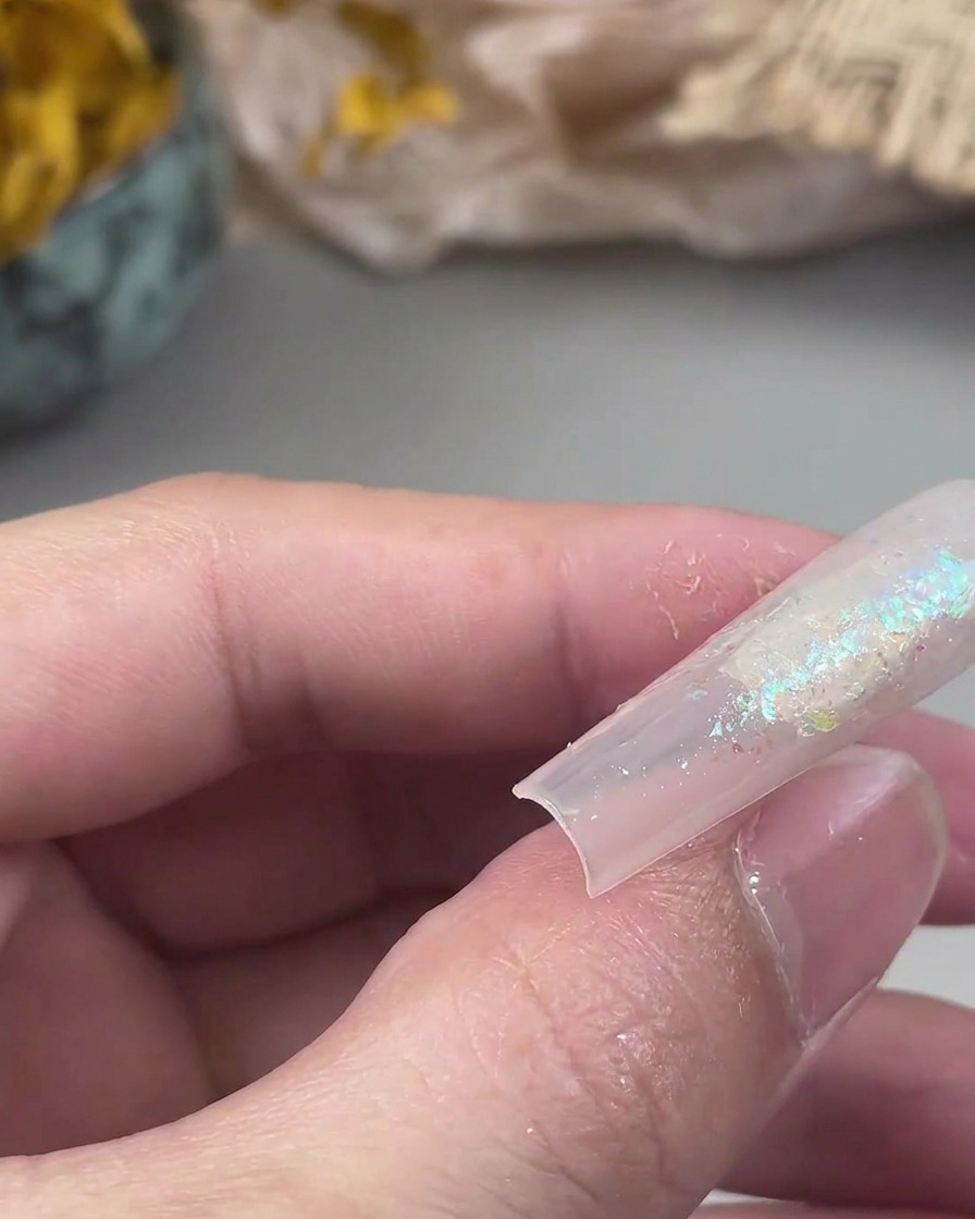Un piccolo pennello piatto preme le particelle di glitter libere su una superficie di gel appiccicosa dellunghia.