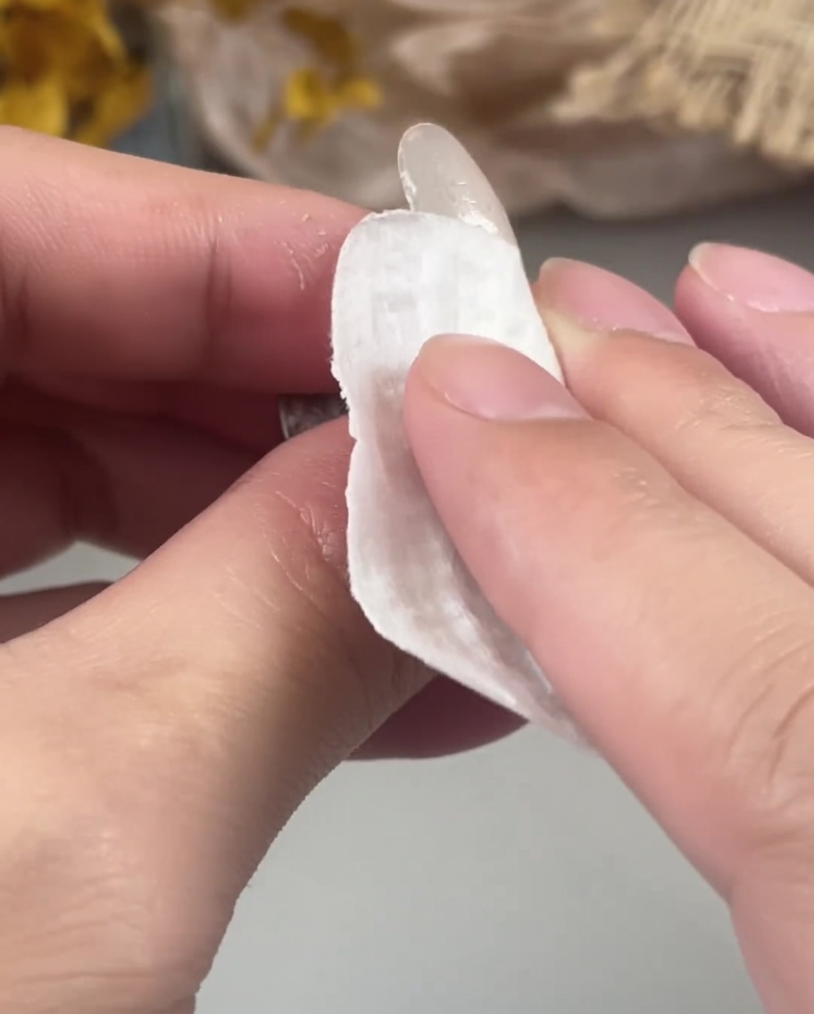 Una mano passa un pad che non lascia pelucchi per pulire la superficie di ununghia in gel appena polimerizzata.