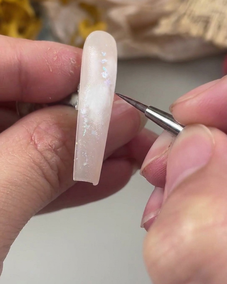 Un pennello liner sottile posizionato sopra larea bianca dipinta sullunghia, pronto a tracciare il delicato centro della rosa ad acquerello.