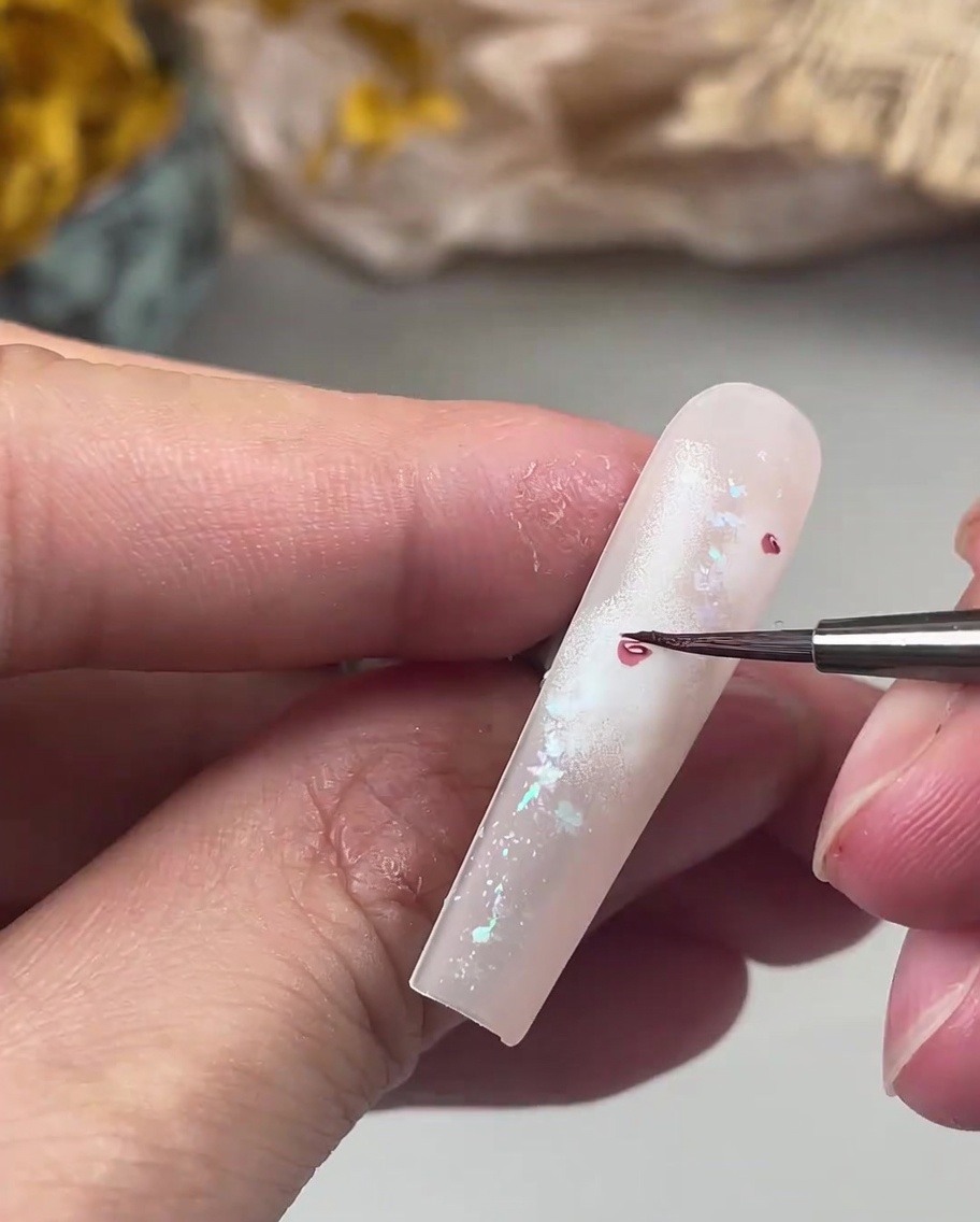 Un pennello da nail art di precisione dipinge piccoli e delicati petali rosa scuro attorno al cuore centrale di una rosa sullunghia.