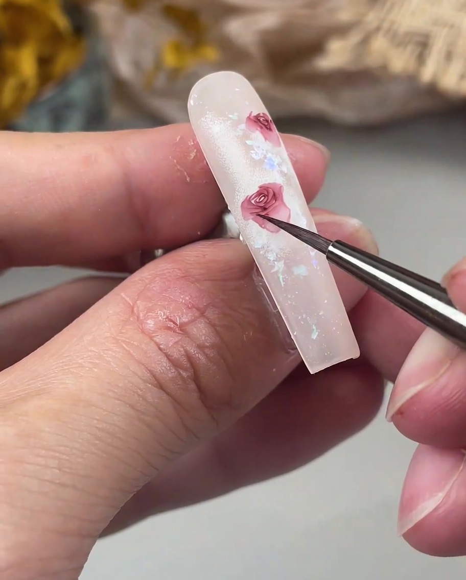 Un pennello di precisione aggiunge delicati petali curvi verso lesterno sul bordo del disegno di una rosa sullunghia.