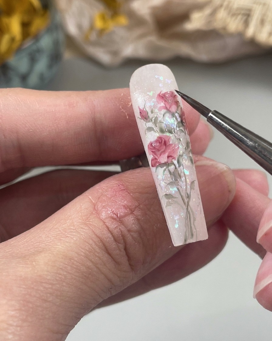 Un primo piano di un pennello fine per nail art che dipinge una piccola goccia dacqua rosa tenue sulla superficie dellunghia come parte di un design floreale.
