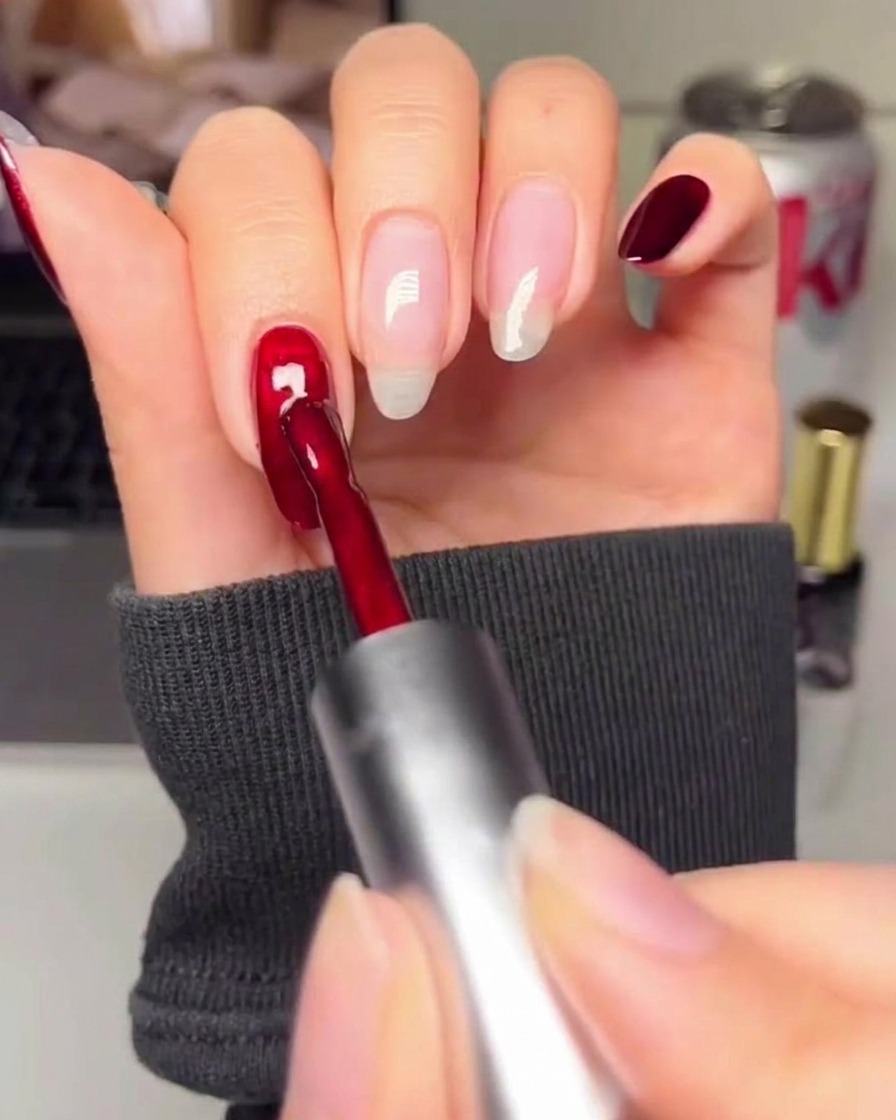 Un primo piano di un pennello che applica uno smalto gel rosso intenso su una superficie ungueale preparata.