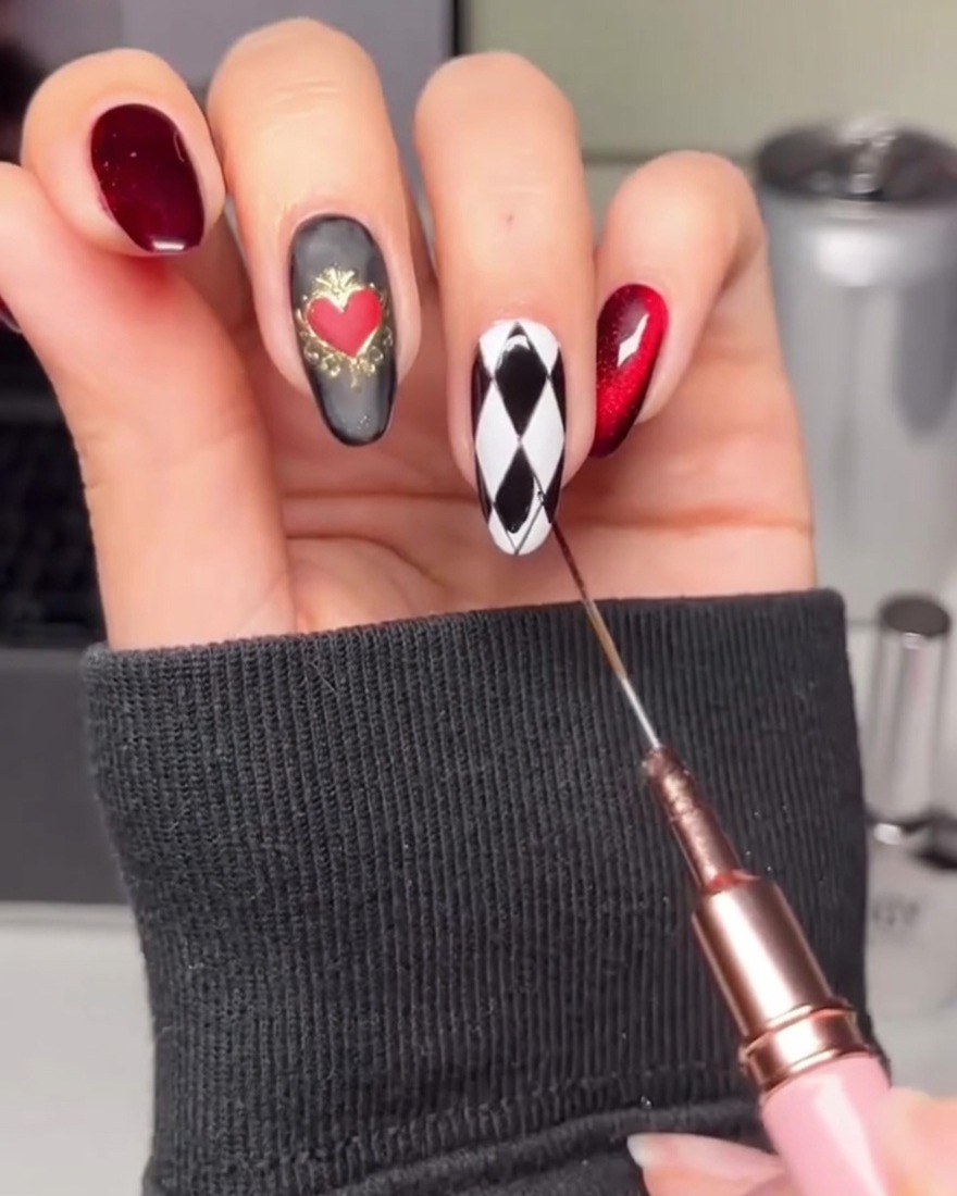 Una mano che usa un pennello liner per riempire forme a rombo alternate su ununghia bianca con gel nero.