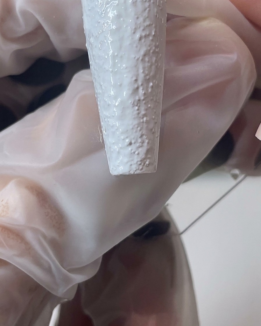 Dettaglio di un pennello che modella il gel effetto sabbia bianco per creare un bordo spesso e testurizzato sullunghia.