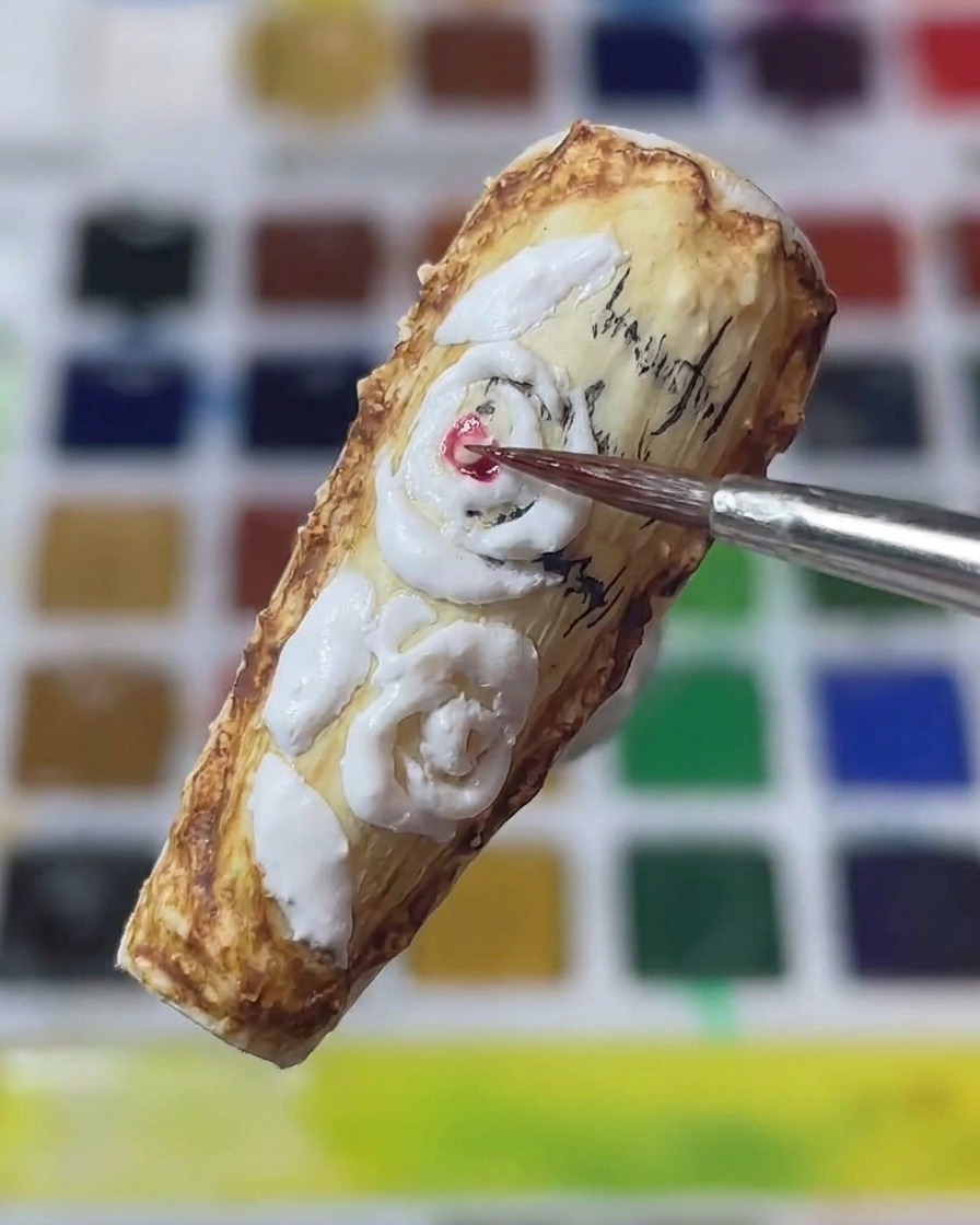Dettaglio di un pennello da nail art che applica pigmento rosso al centro di rose bianche scolpite 3D su ununghia in stile vintage.