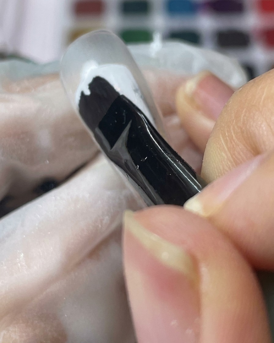 Un pennello per gel nero applica uno strato uniforme di gel bianco su una tip trasparente.