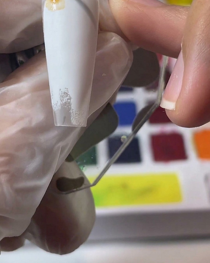 Una mano che tiene una tip bianca mentre mescola e applica pigmenti color acquerello marrone.