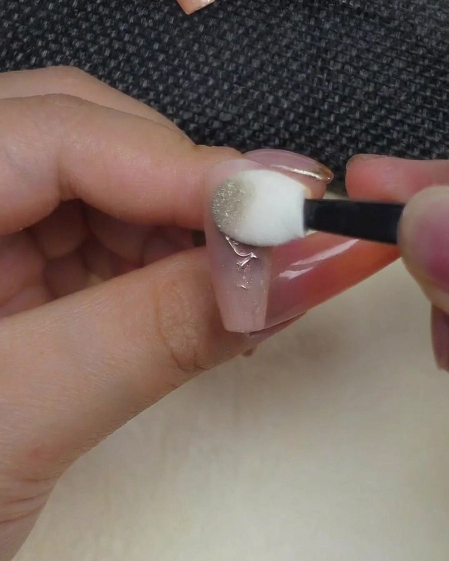 Un applicatore in spugna stile ombretto che pressa la polvere cromata metallizzata su un design a rosa in rilievo.