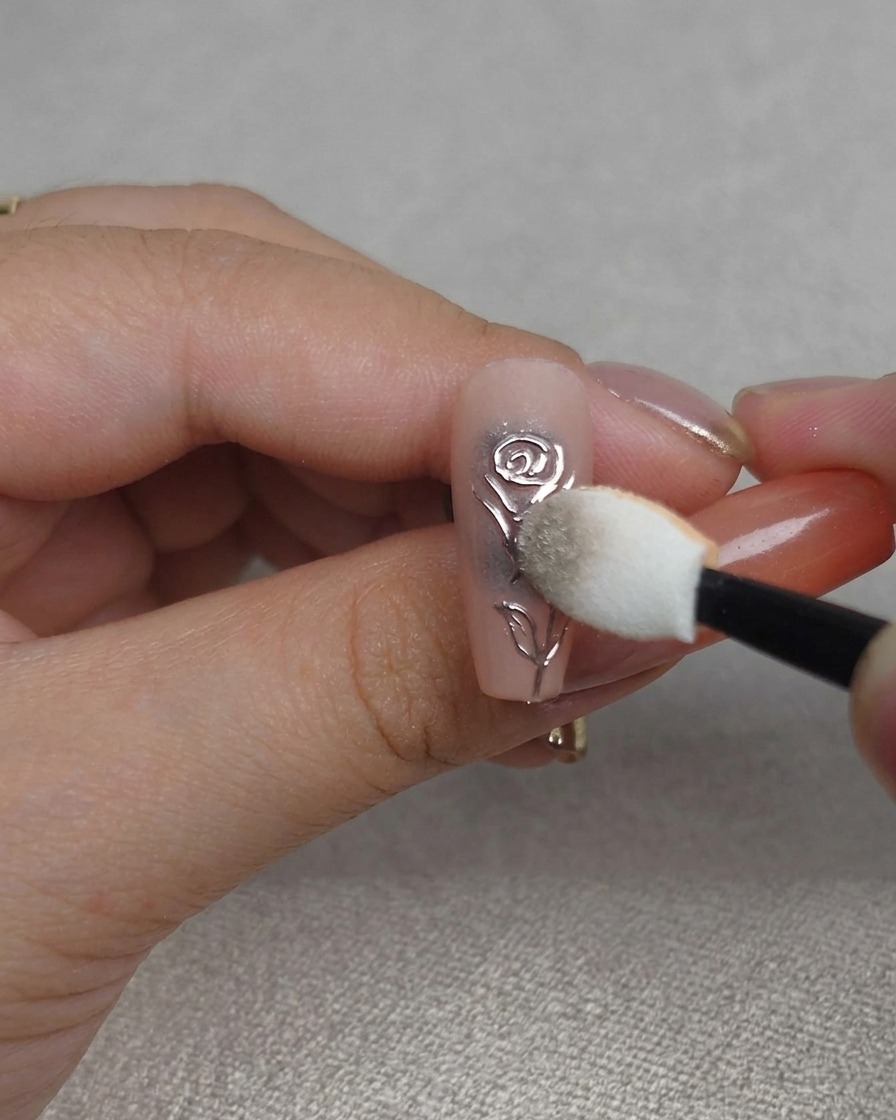 Primo piano di una spugnetta che lucida la polvere cromata nei solchi di un design 3D a rosa, creando una finitura metallizzata estremamente brillante.