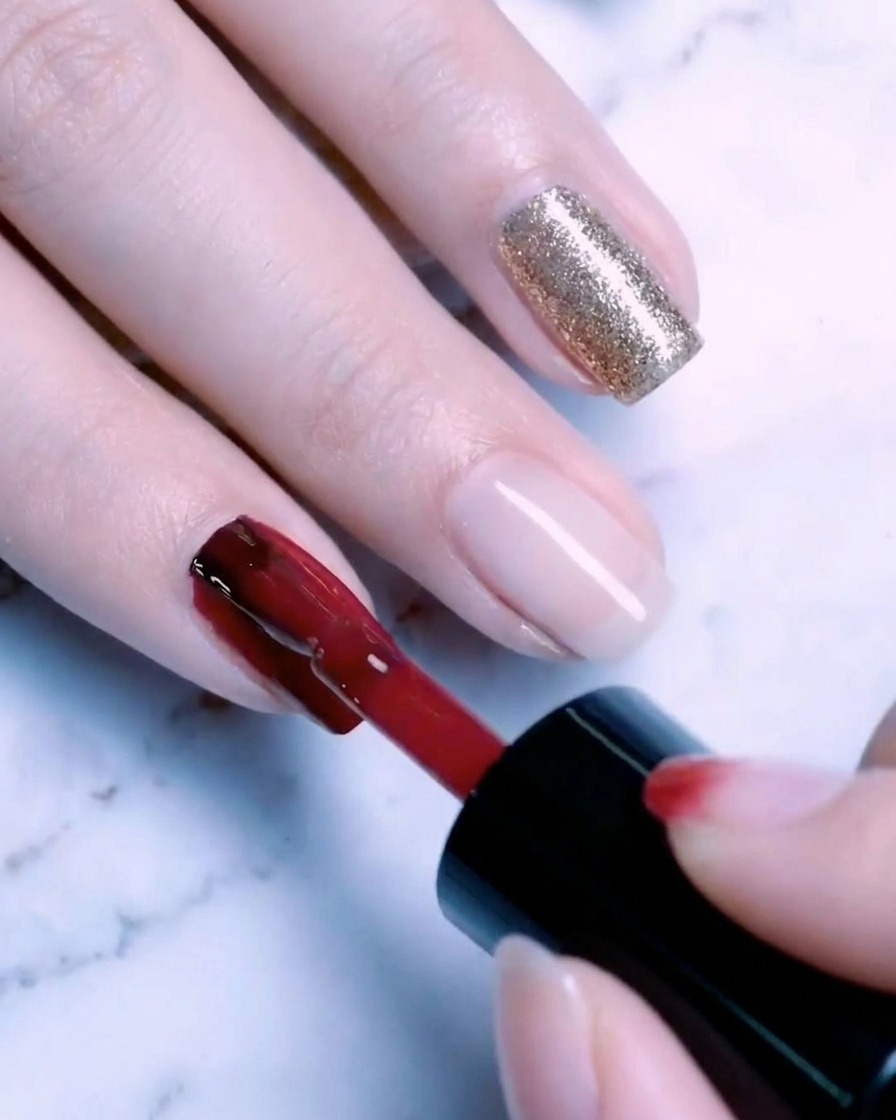 Un pennello che applica un secondo strato di gel glitter oro sullunghia, creando una finitura ricca e scintillante.