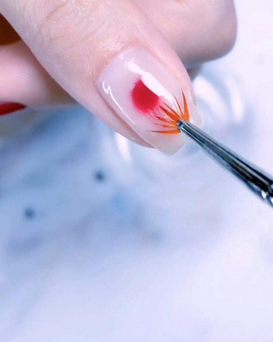 Primo piano di ununghia del pollice con una base bianco latte e una goccia centrale di smalto gel rose gold sfumata verso lesterno con un pennello a ventaglio.