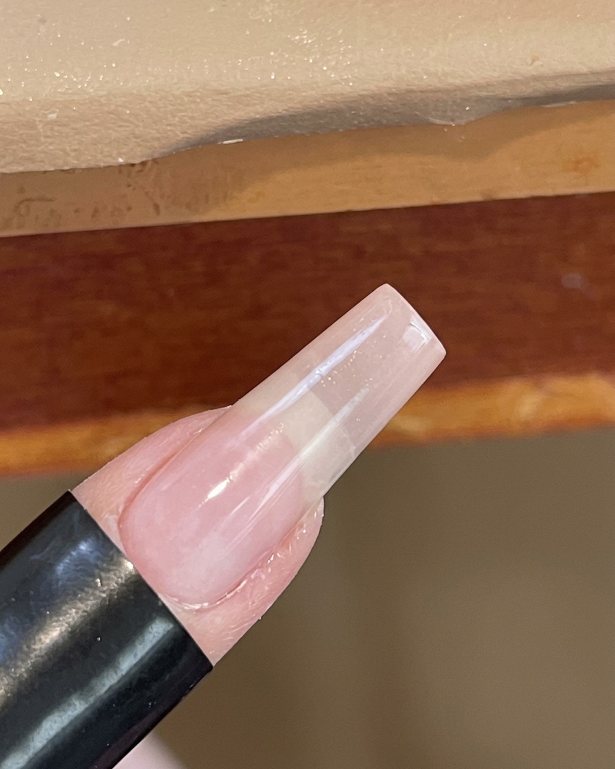 Primo piano di ununghia che polimerizza sotto una piccola lampada UV/LED portatile bianca.