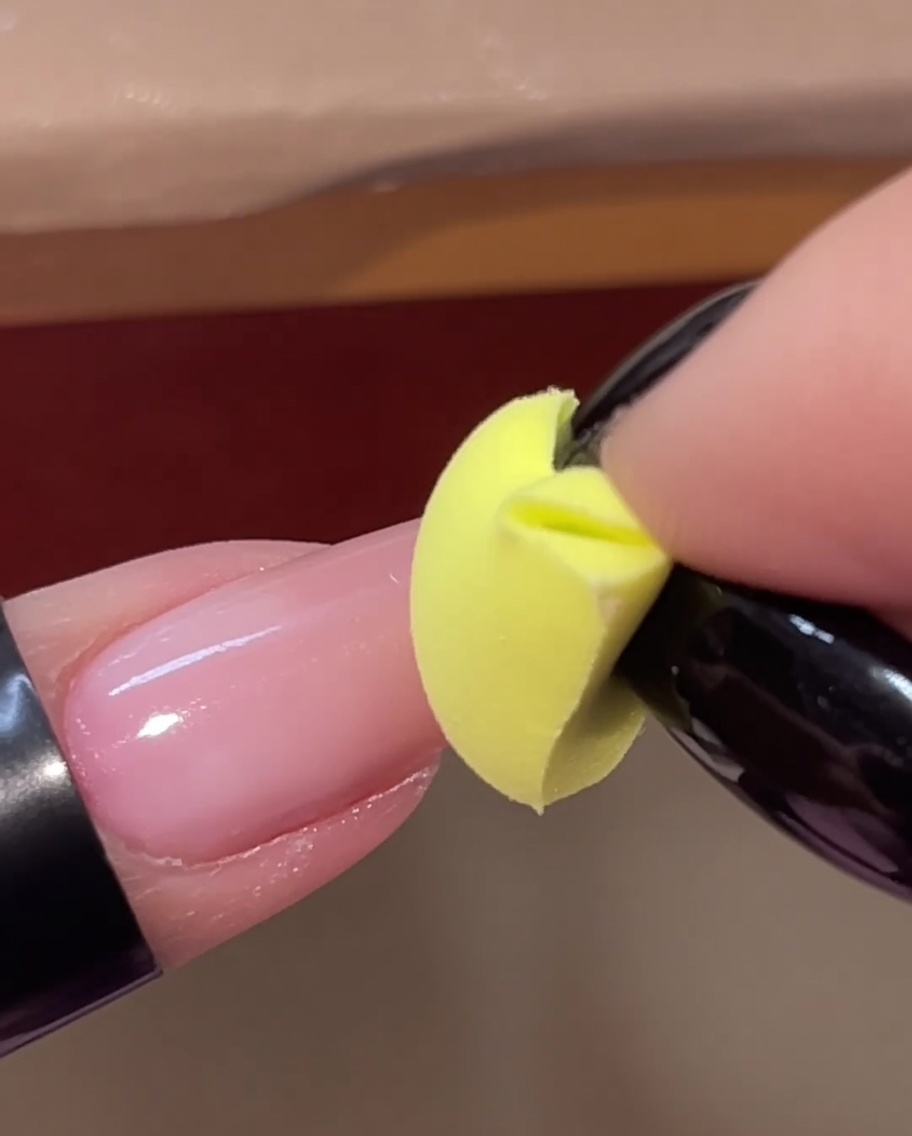 Una spugnetta gialla che picchietta un secondo strato di gel rosa sulla punta di ununghia.