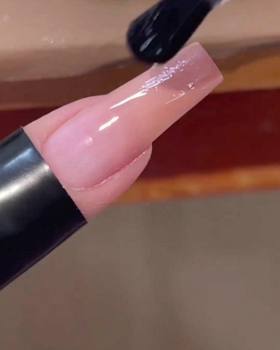 Un pennello applica un top coat trasparente e lucido sullunghia sfumata rosa finita.