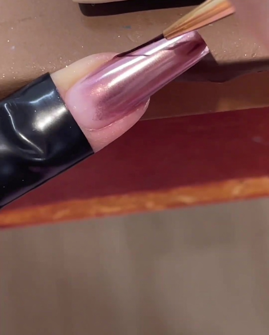 Un pennello sottile da nail art applica una linea trasparente di gel costruttore diagonalmente su ununghia cromata.