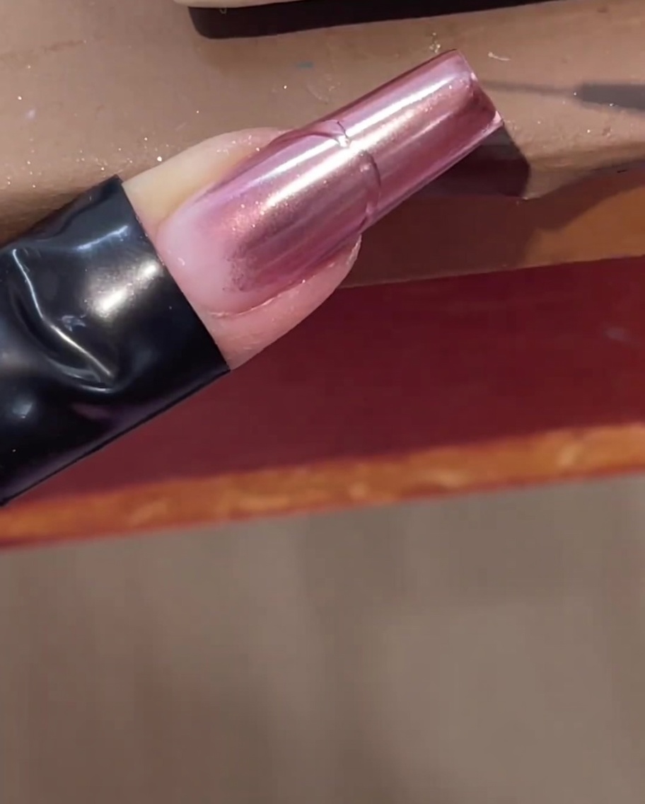 Un pennello liner sottile disegna una linea in rilievo in gel trasparente su ununghia cromata rosa.