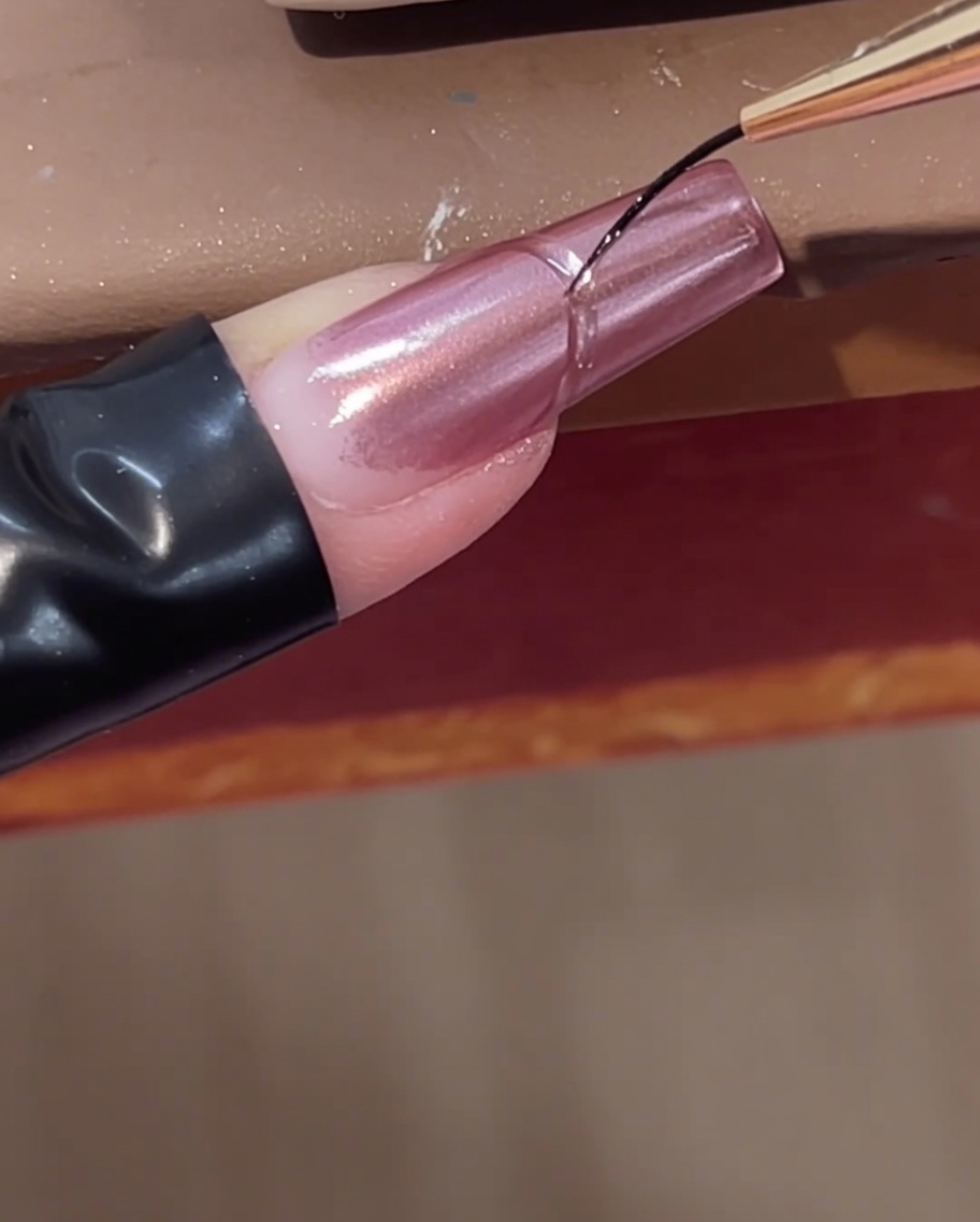 Un pennello liner sottile aggiunge una linea curva di gel costruttore trasparente vicino alla cuticola di ununghia cromata rosa.