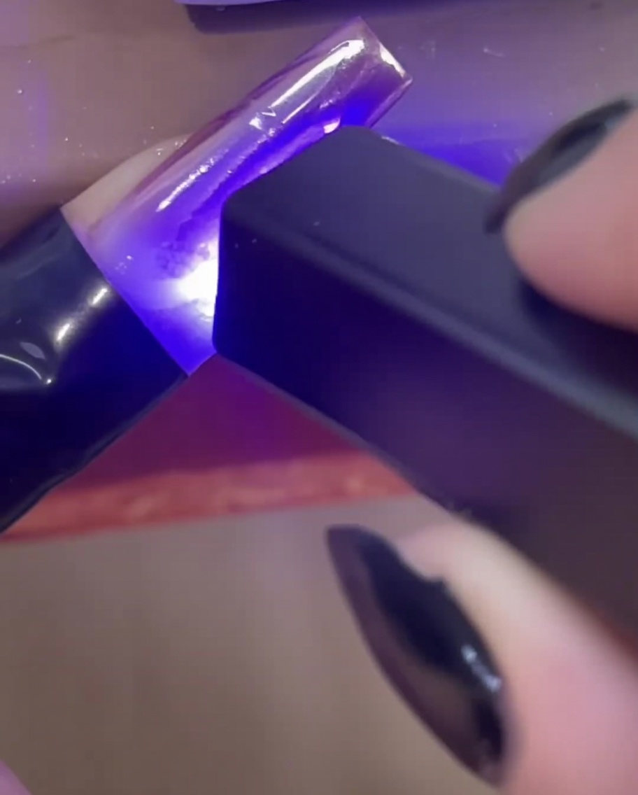 Una mini lampada UV/LED portatile polimerizza le linee 3D trasparenti di gel costruttore su unestensione dellunghia.
