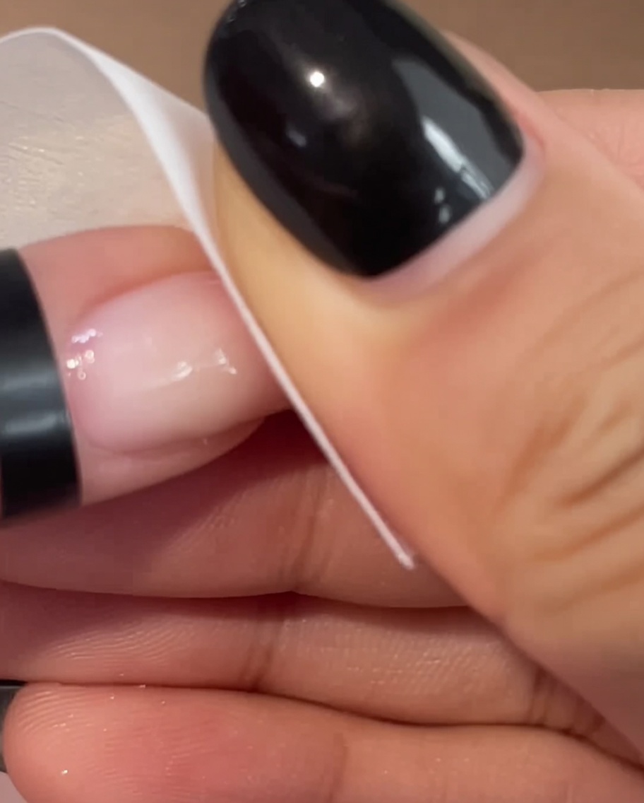 Primo piano di una mano che utilizza un pad bianco per pulire delicatamente la superficie di ununghia rosa appena fatta.