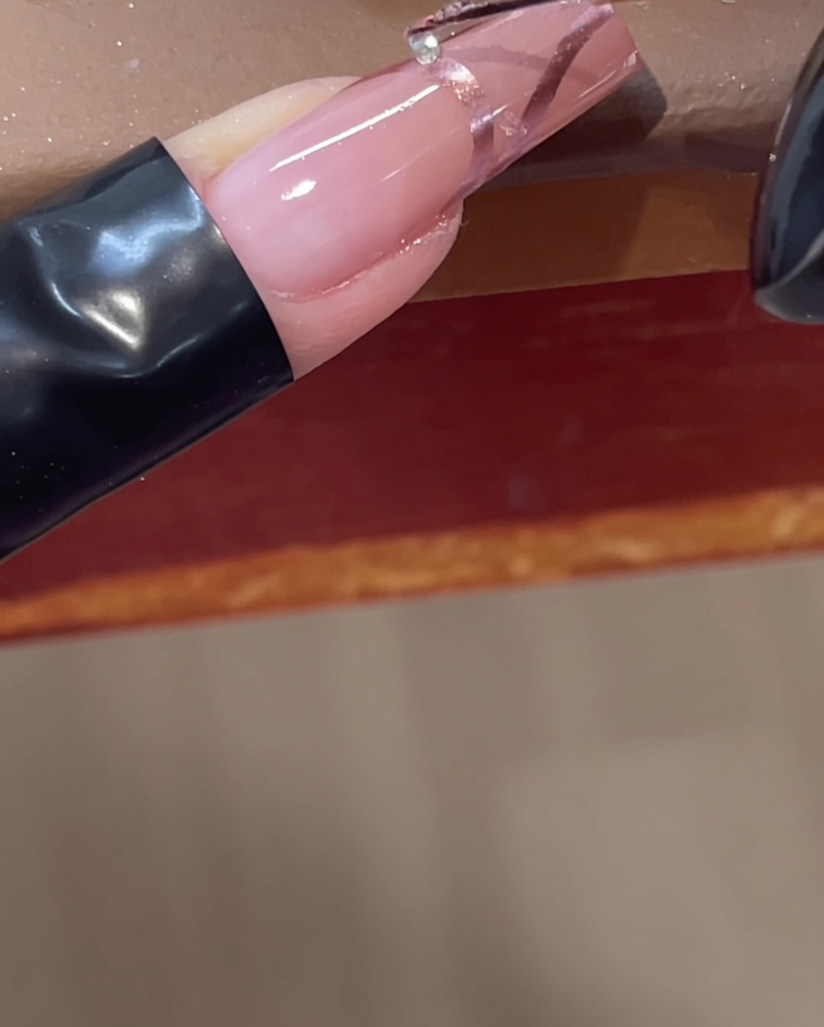 Posizionamento di un piccolo strass trasparente su una linea cromata 3D su ununghia rosa utilizzando uno strumento.
