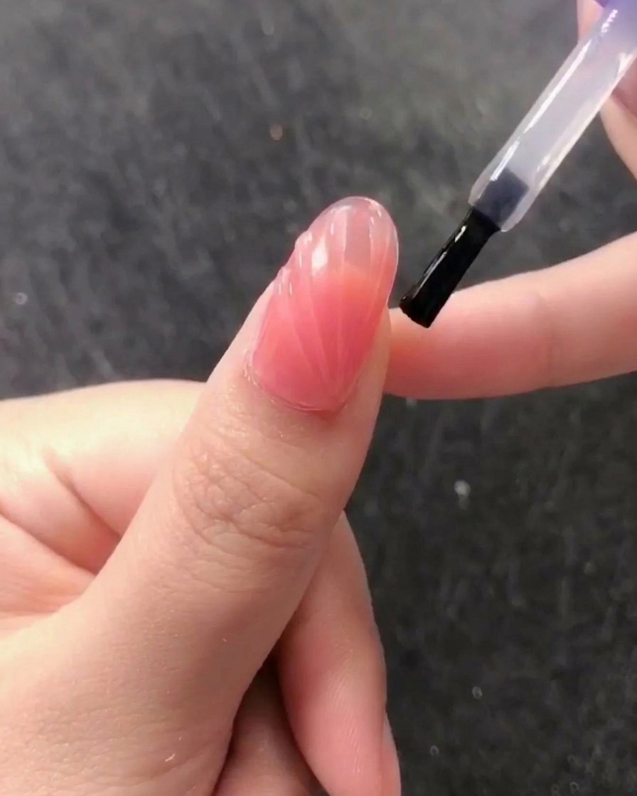 Un pennello stende un top coat trasparente e lucido senza dispersione sopra il design a conchiglia in rilievo.