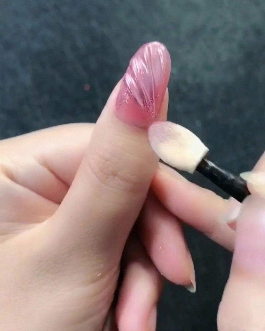Un applicatore per ombretto lucida la polvere cromata oro rosa sulla superficie strutturata dellunghia.