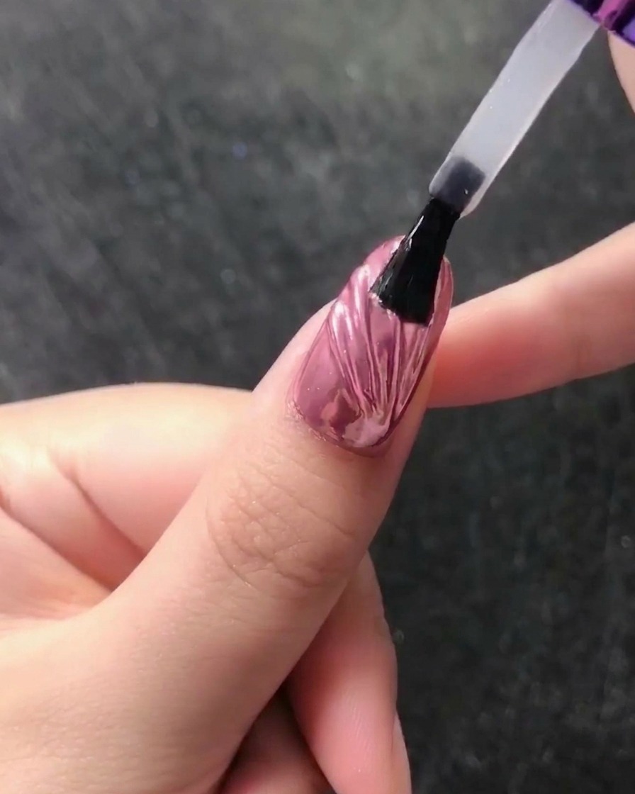 Primo piano di una matita in cera che posiziona una piccola perla bianca alla base di ununghia cromata.