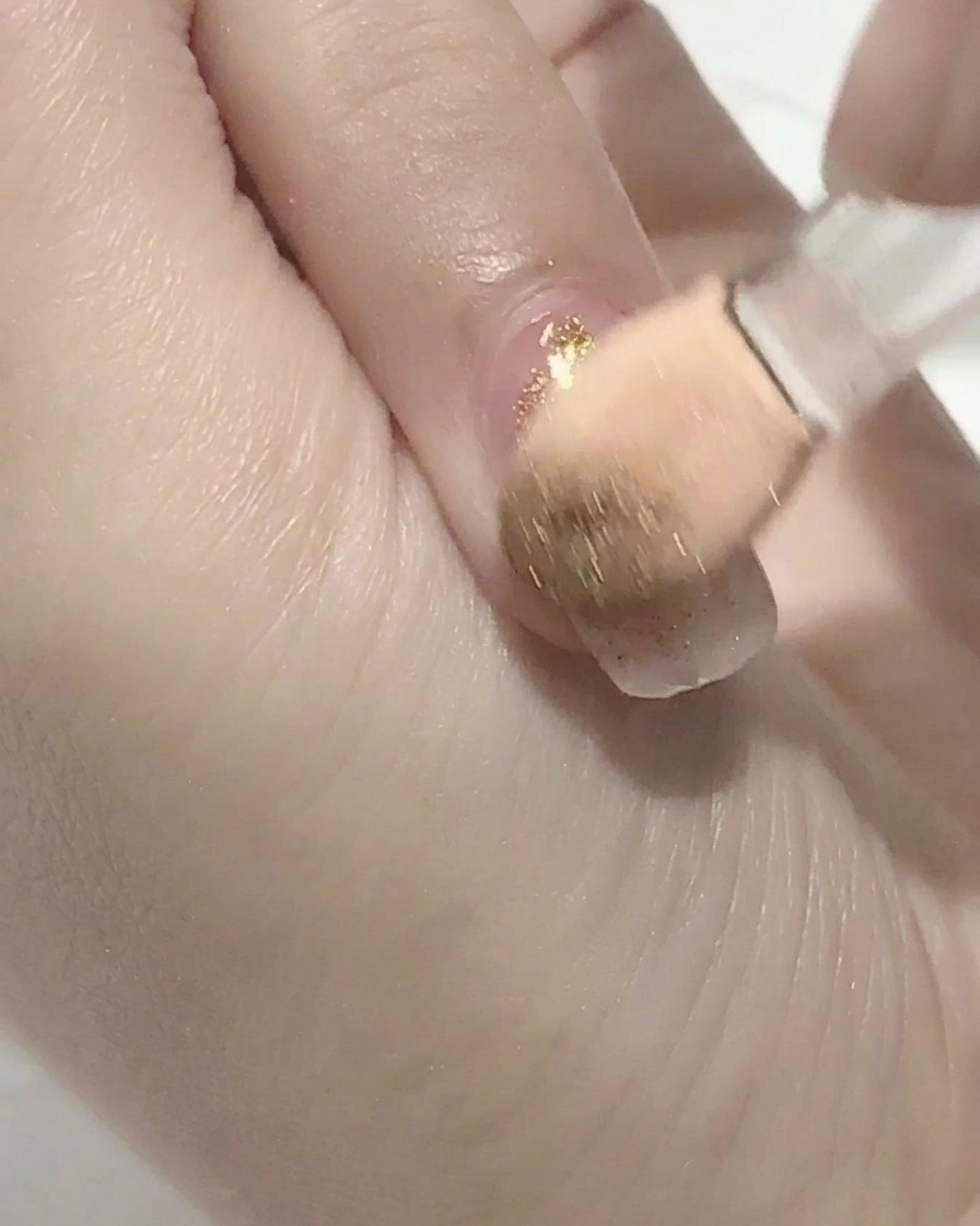 Un pennello applica top coat trasparente su ununghia in gel rosa.
