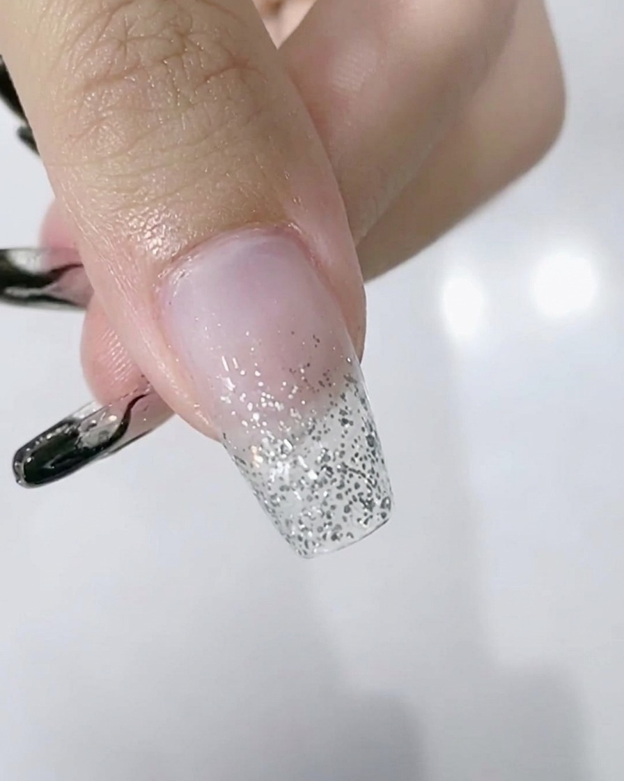 Primo piano di una mano con sfumato glitter argento sulle unghie posizionata allinterno di una lampada LED.