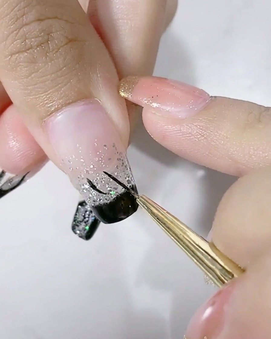Un pennello liner sottile che disegna un contorno a U nero sulla parte glitter argento di ununghia.