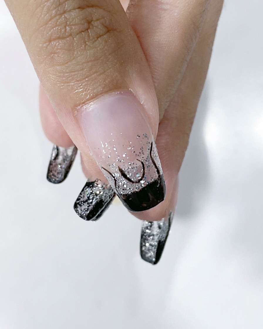Primo piano di ununghia che mostra il contorno della fiamma nera completato su una base sfumata glitter argento.