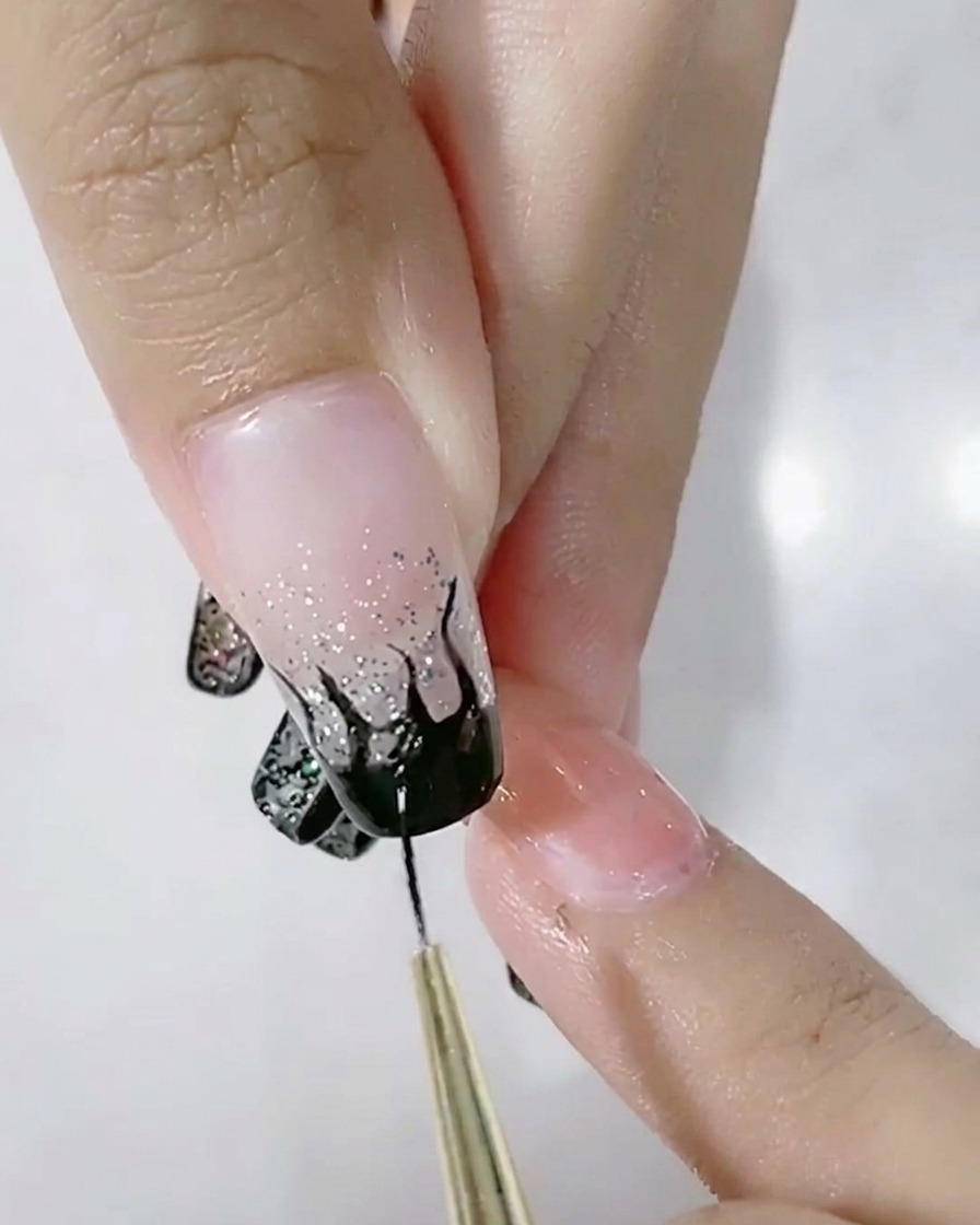 Un pennello liner che riempie un design a fiamma nera su ununghia sfumata glitter.