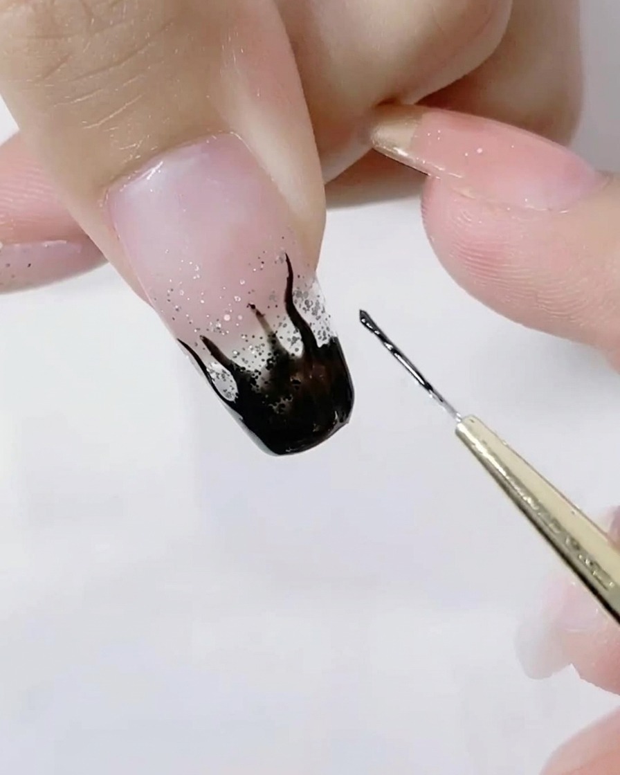 Primo piano di un pennello liner che dettaglia le punte affilate di fiamme nere su ununghia glitter.