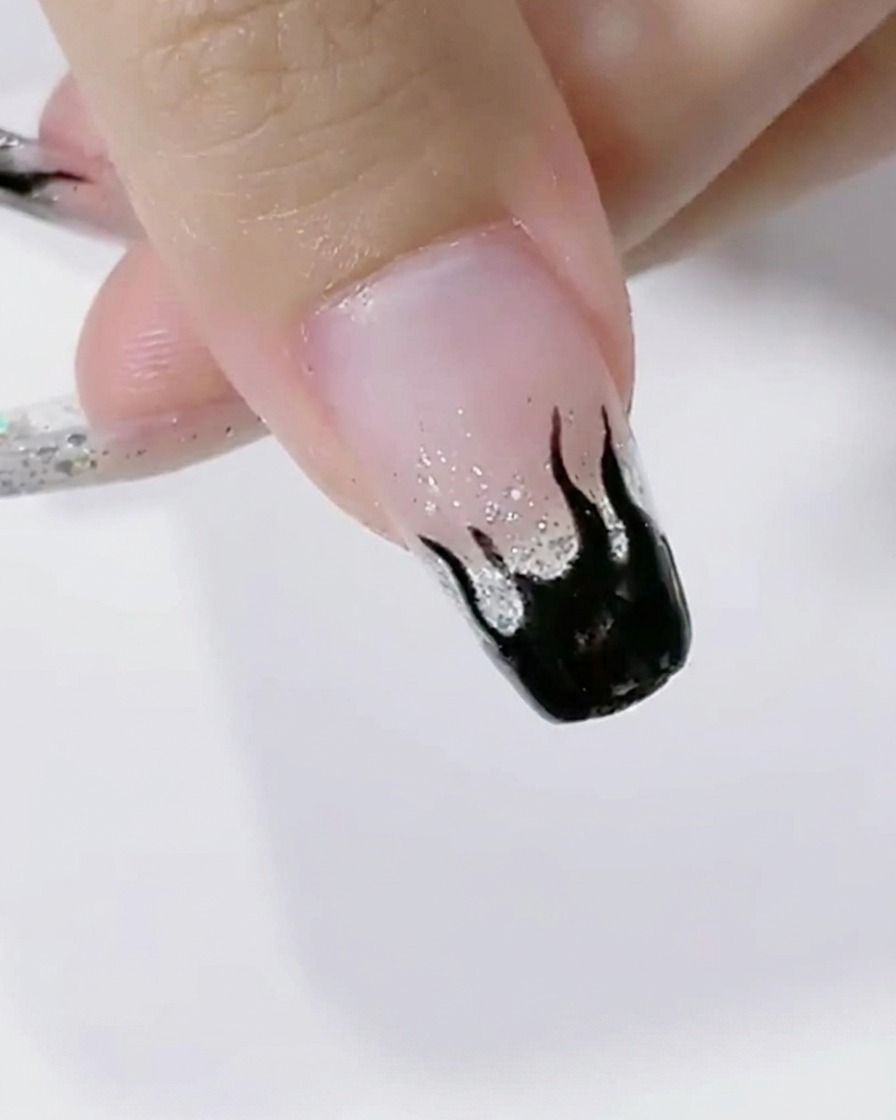 Unghie con nail art a fiamma nera che polimerizzano sotto la luce intensa di una lampada LED.