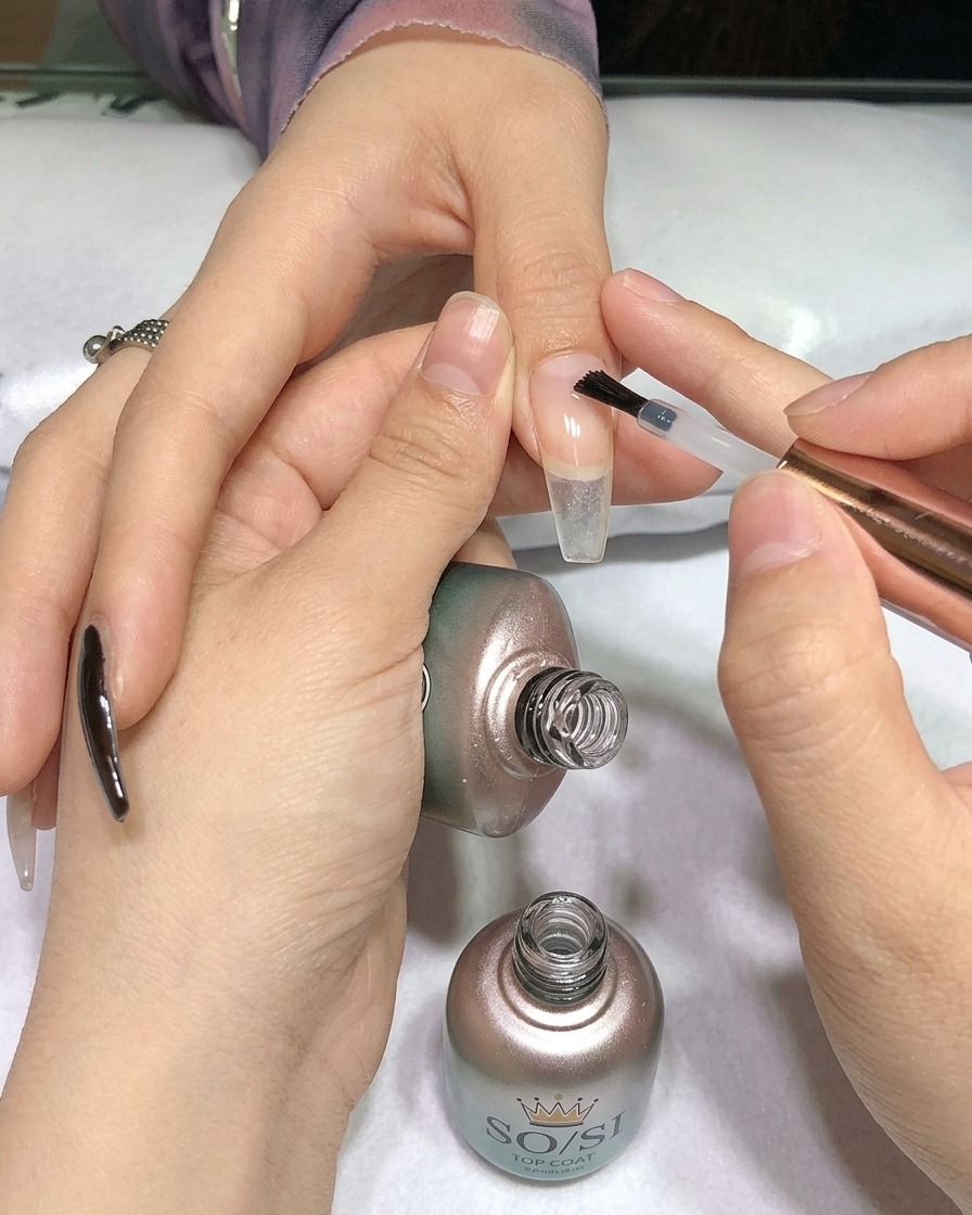 Un pennello applica un top coat trasparente sopra ununghia dipinta di nero.