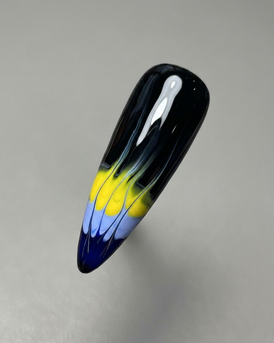Un pennello a punta sottile trascina i gel blu e gialli verso lalto per creare la base del motivo a fiamma.