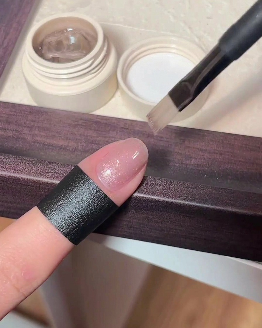 Vista ravvicinata dellapplicazione di un gel cat-eye rosa brillante su ununghia naturale.