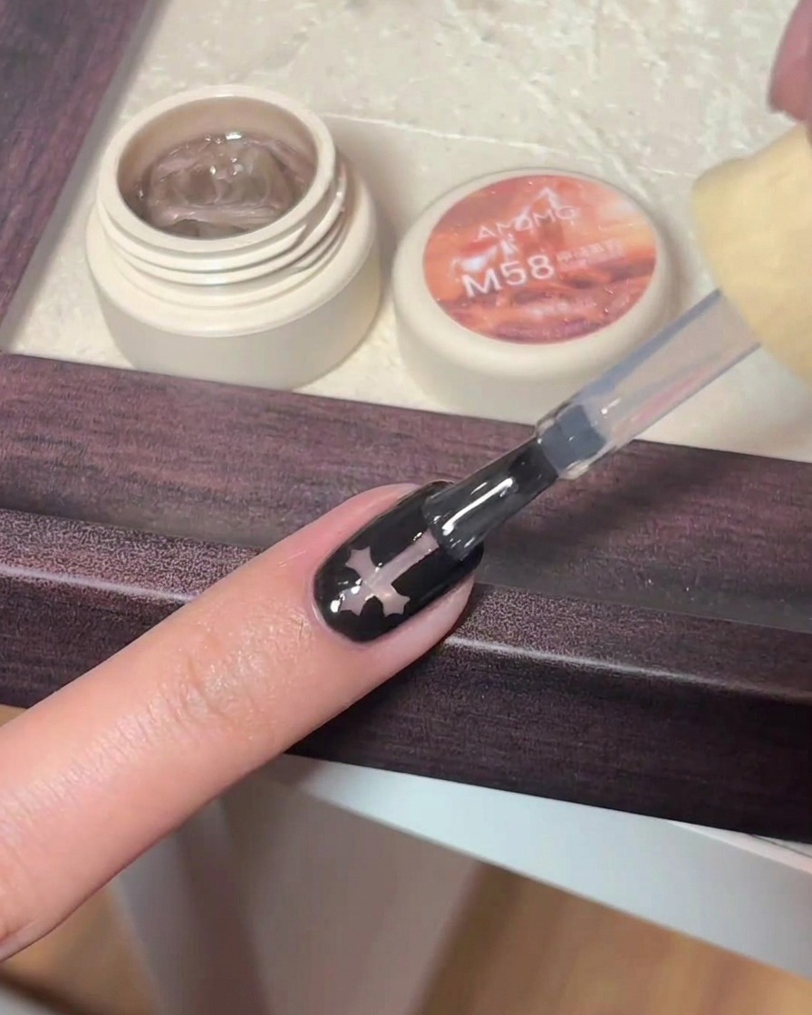 Pennello che applica un top coat lucido su ununghia nera con croce.