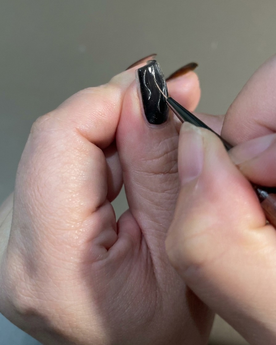 Un primo piano di un pennello liner che assottiglia le estremità dei design a fiamma su ununghia per creare una finitura affilata e irregolare.