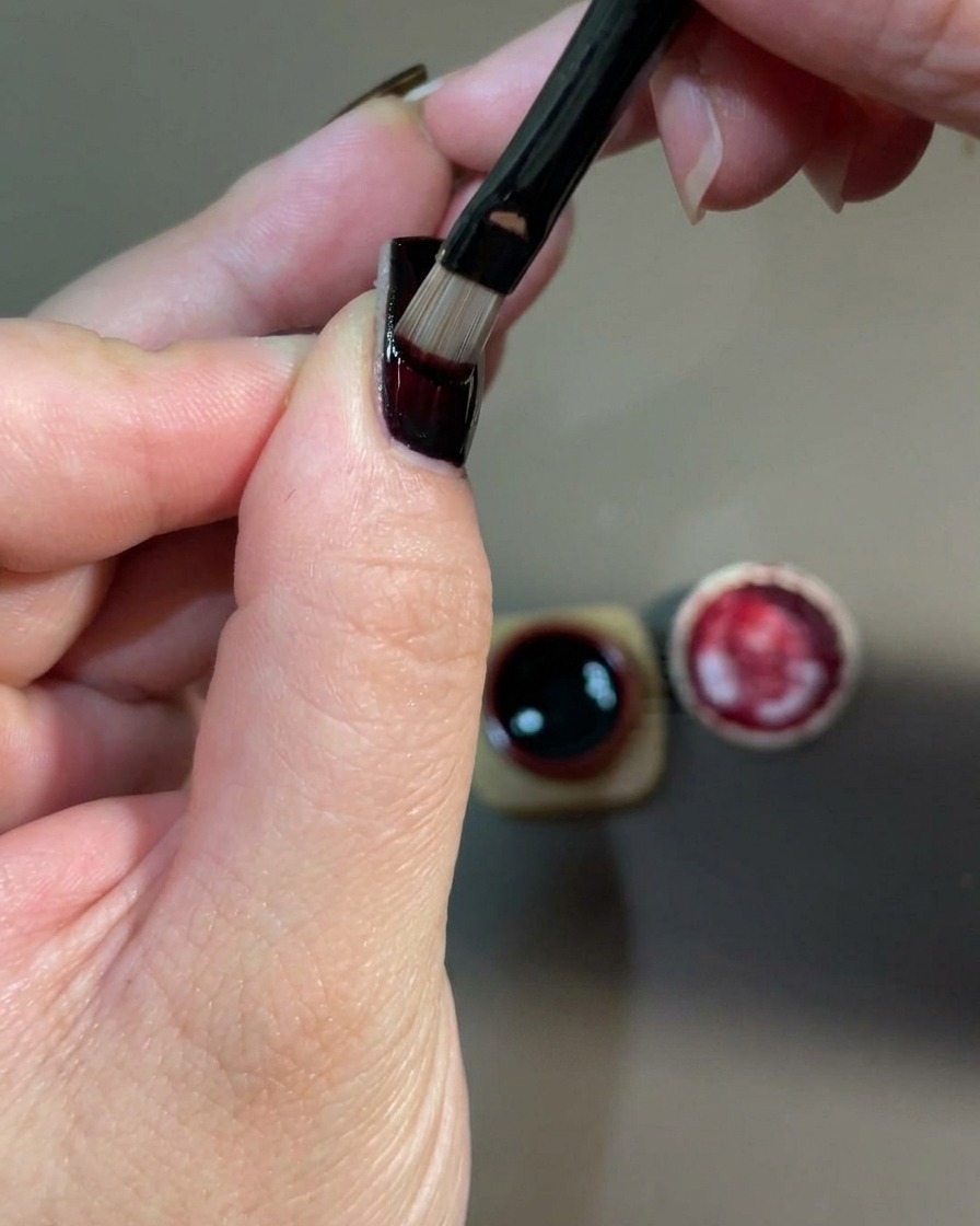 Un primo piano di una mano allinterno di una lampada UV per unghie per polimerizzare lo strato di gel rosso appena applicato.