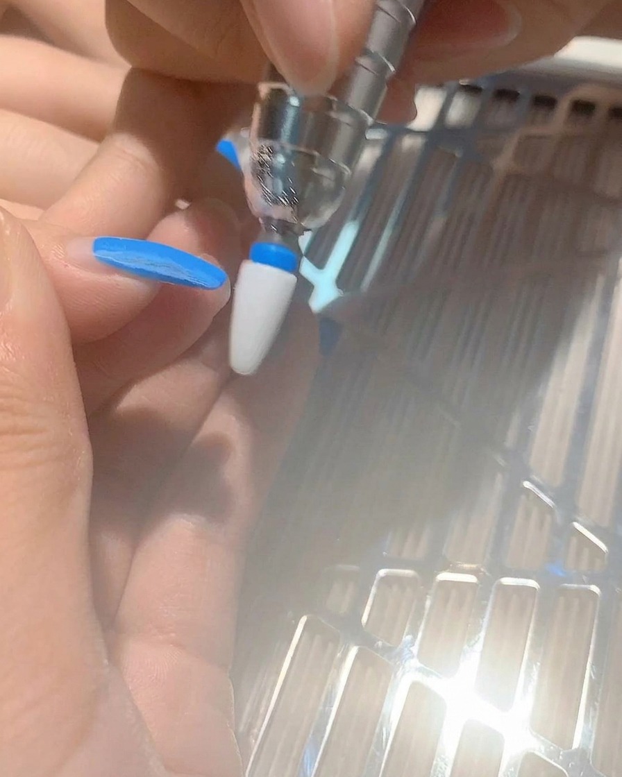 Un primo piano di una fresa per unghie che rimuove lo smalto gel blu da ununghia.
