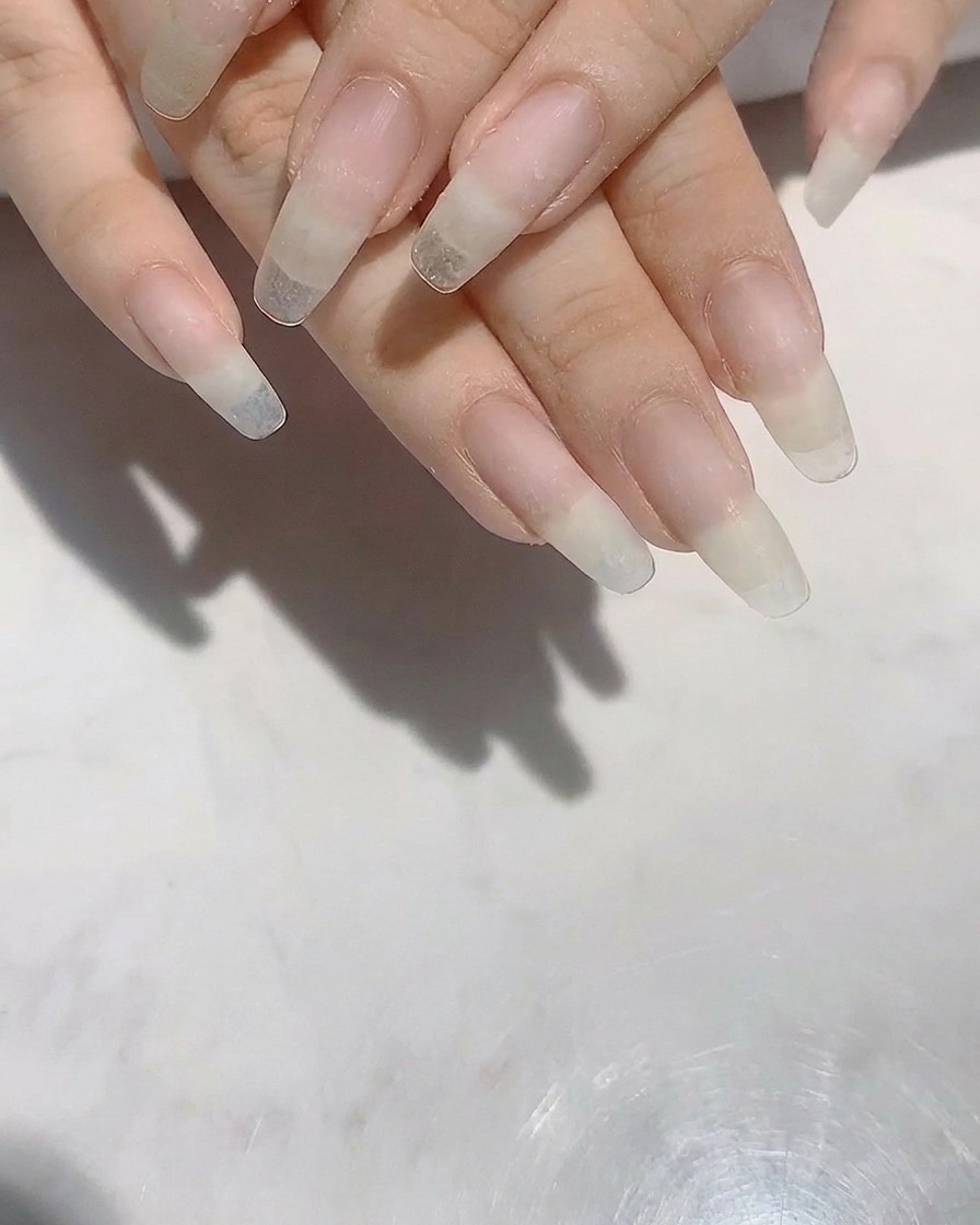 Un paio di mani con unghie naturali lunghe e modellate, in fase di limatura.