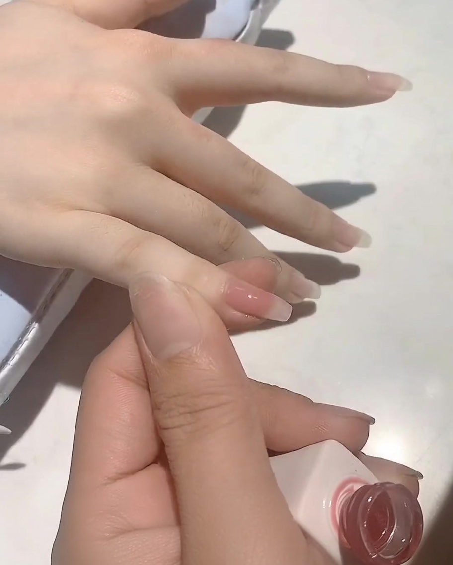 Un pennello che applica uno smalto gel color rosa carne delicato su ununghia naturale.