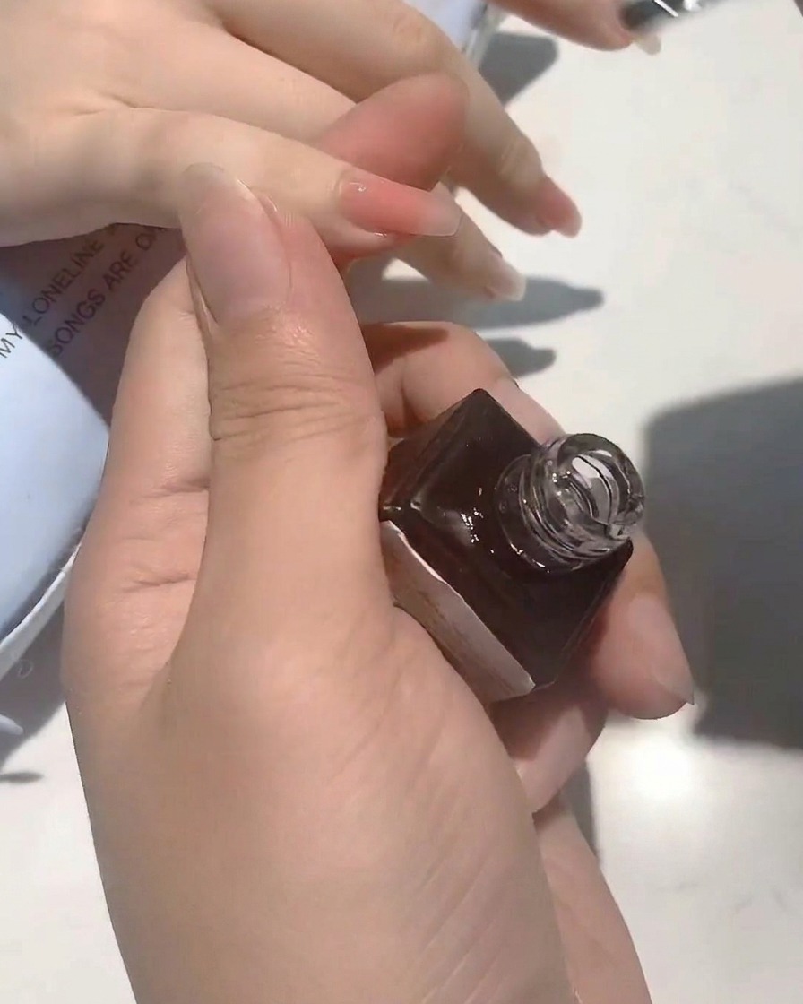 Un primo piano di un pennello che applica un top coat trasparente e lucido su ununghia dal colore neutro.