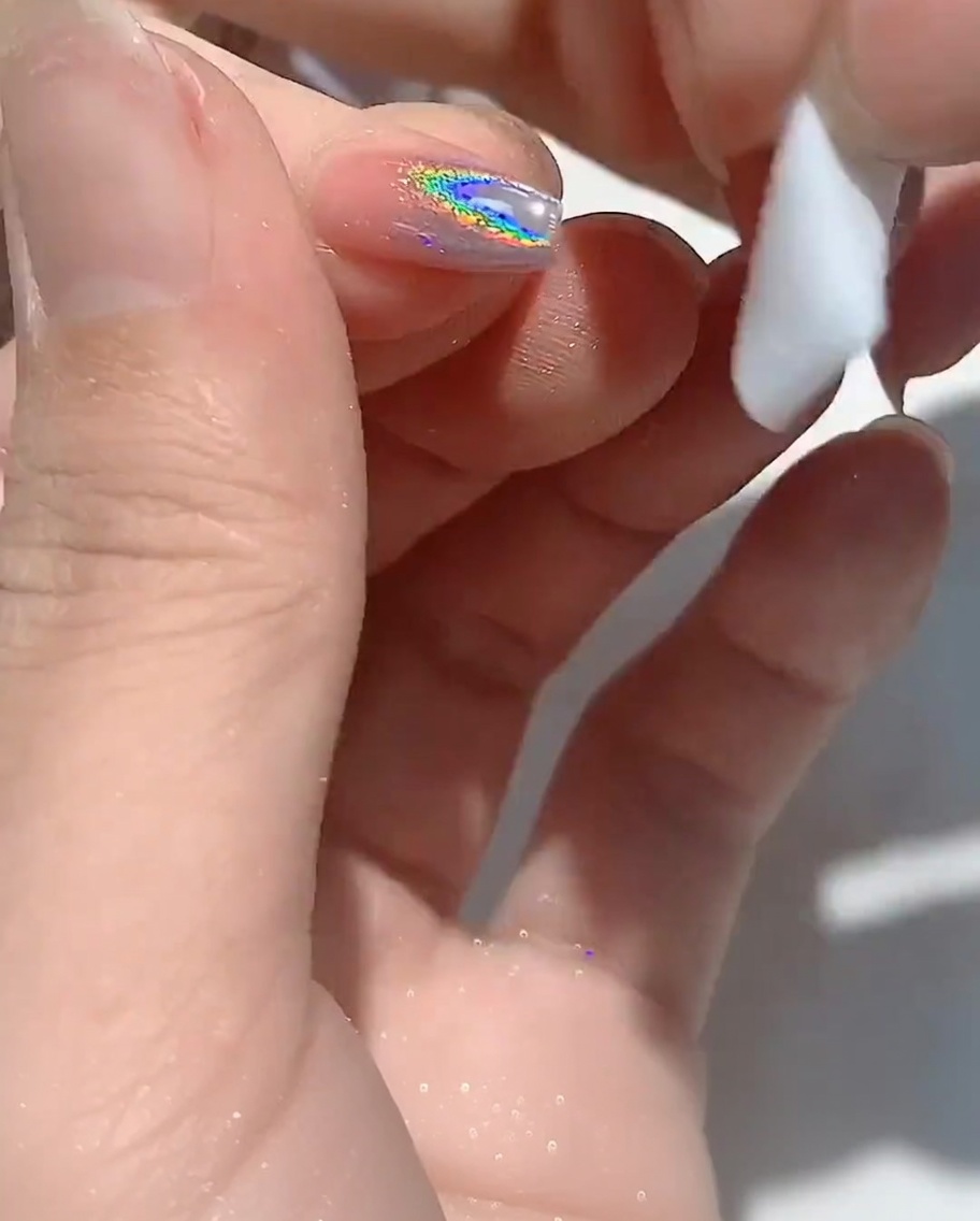 Un pad di cotone senza pelucchi che pulisce il bordo di ununghia.