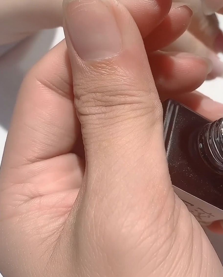 Un pennello che stende una base coat in gomma densa e trasparente su ununghia con dettagli iridescenti.