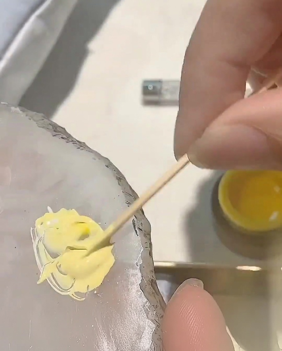 Una piccola goccia di smalto gel rosso aggiunta alla miscela di gel giallo esistente su una tavolozza.